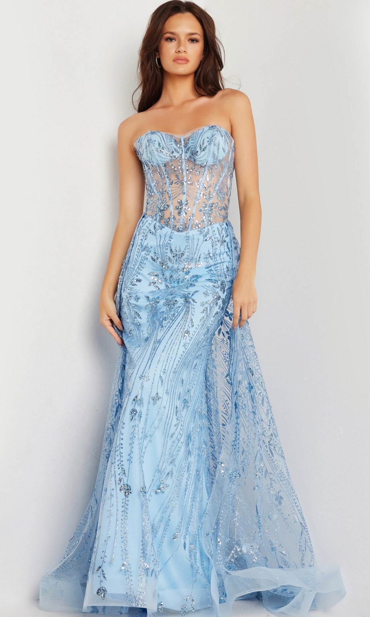 A woman models the Jovani Strapless Long Glitter-Sequin Prom Dress 26113 in light blue, featuring a strapless sheer corset-style bodice and mermaid skirt, standing against a plain background.